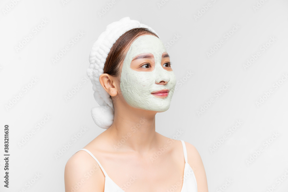 Portrait of beautiful young Asian woman with clay mask and towel on her hear over white background.