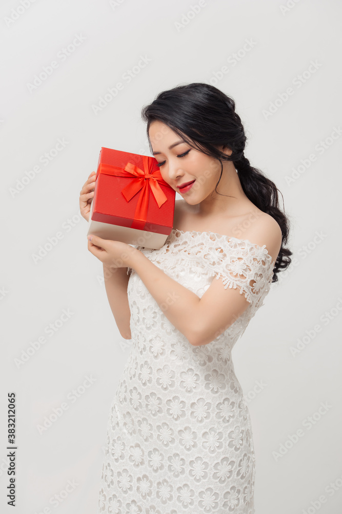 Happy young elegant Asian woman holding special gift box and wearing dress over white background.