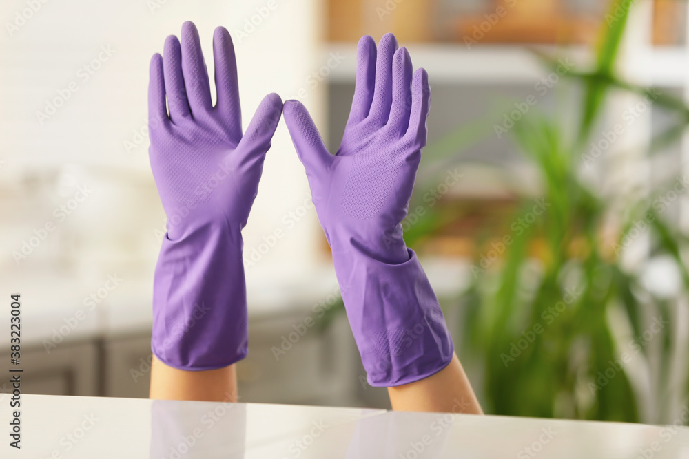 Hands of woman in rubber gloves hiding behind counter in kitchen