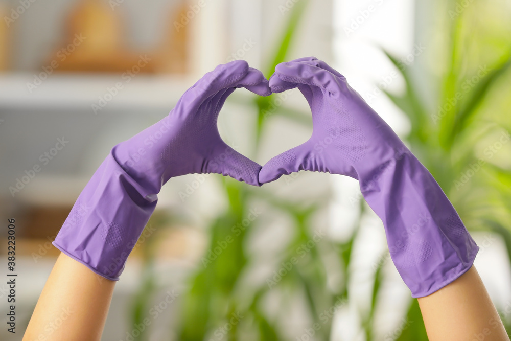 Woman in rubber gloves making heart with her hands at home