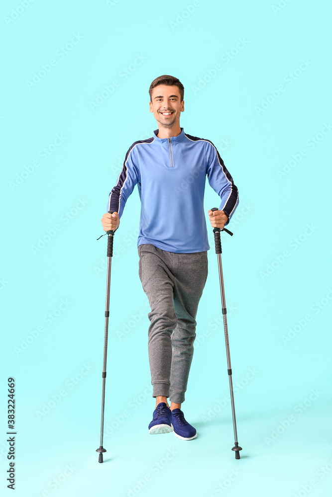 Young man with walking poles on color background