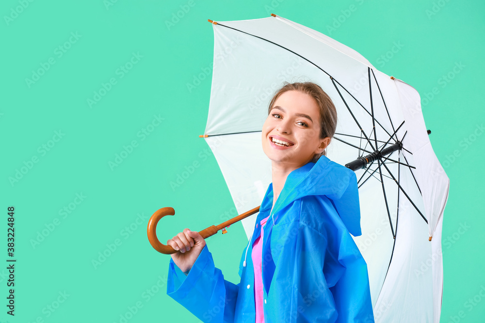 Beautiful young woman in raincoat and with umbrella on color background