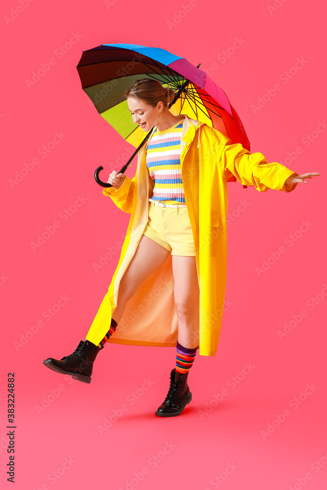 Beautiful young woman in raincoat and with umbrella on color background