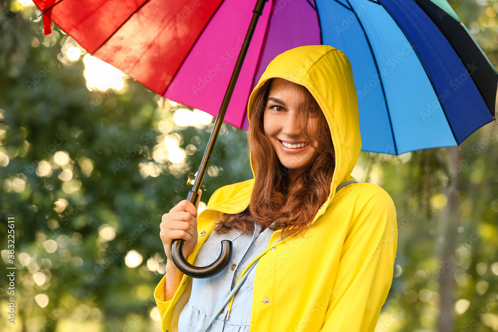 Beautiful young woman with umbrella wearing raincoat in park