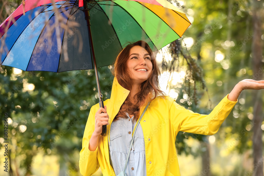 Beautiful young woman with umbrella wearing raincoat in park