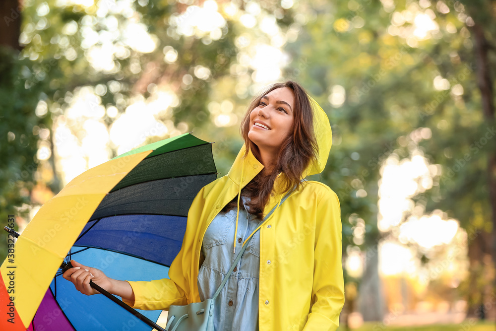 Beautiful young woman with umbrella wearing raincoat in park