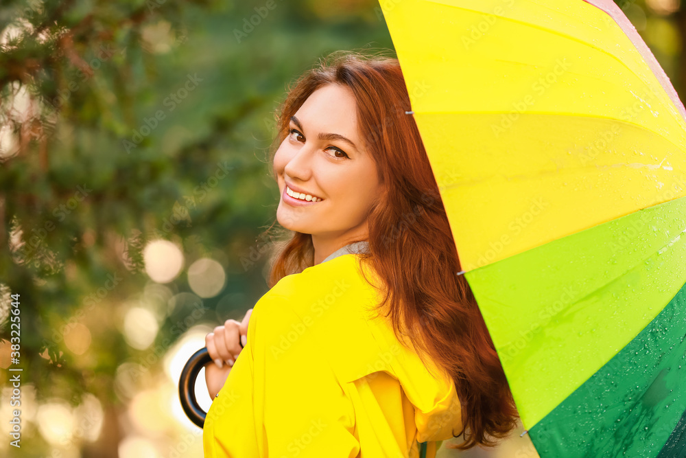 Beautiful young woman with umbrella wearing raincoat in park