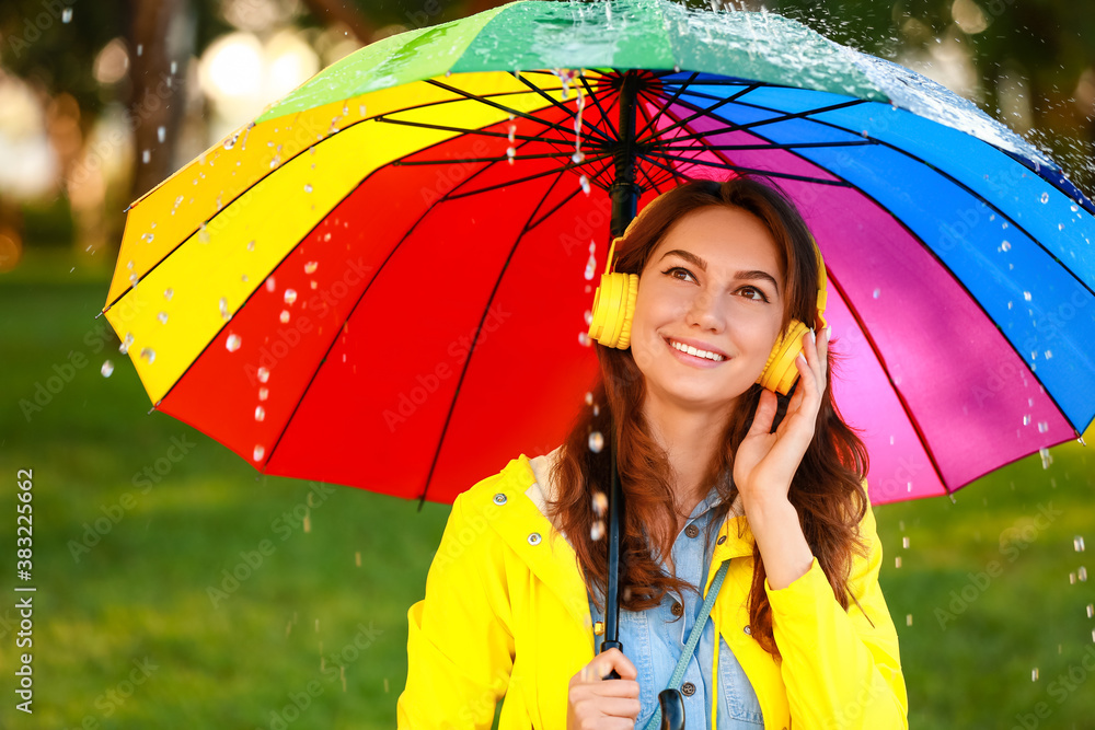 美丽的年轻女子在公园里打着雨伞，穿着雨衣