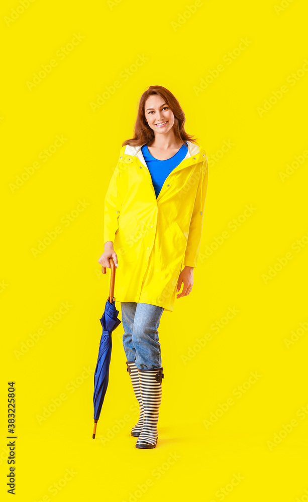 Beautiful young woman in raincoat and with umbrella on color background