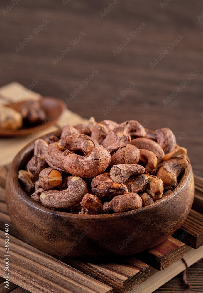 Cashew nuts with peel in a wooden bowl on wooden tray and table background, healthy raw food plate.