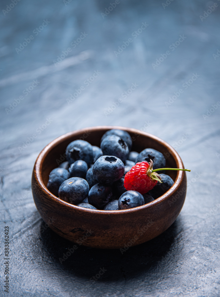 Fresh and sweet blueberry in  wooden bowl with raspberry on dark background