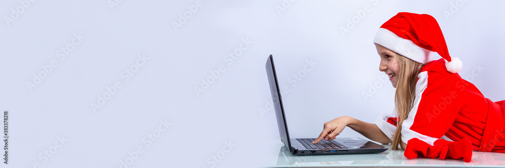 The girl in red Santa uniform is shopping online. White background with laptop. Christmas greetings 