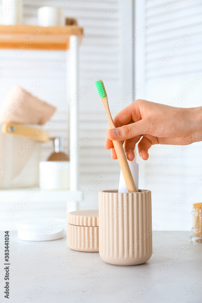 Woman taking tooth brush from cup in bathroom