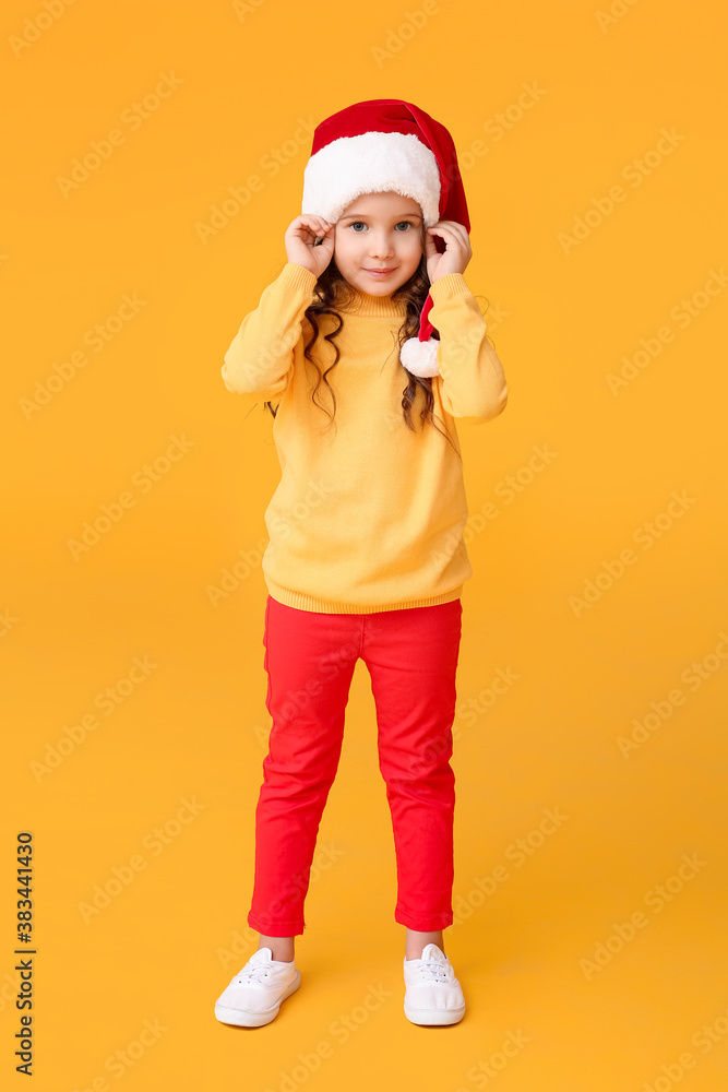 Cute little girl in Santa hat on color background