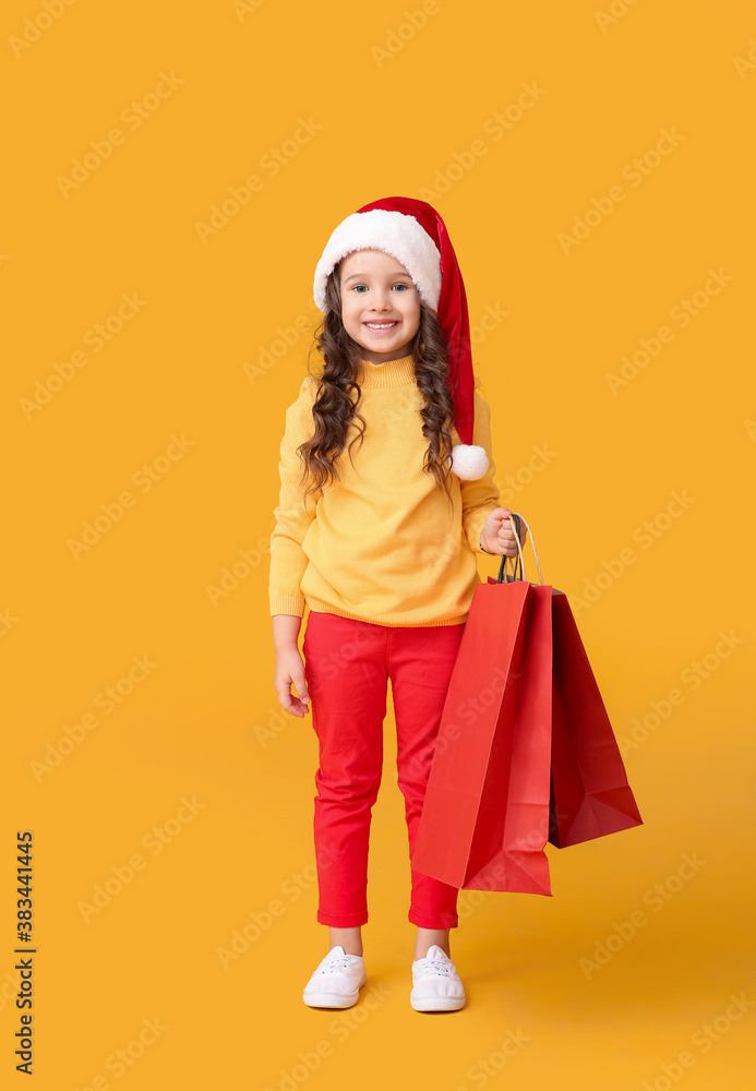 Cute little girl in Santa hat and with shopping bags on color background