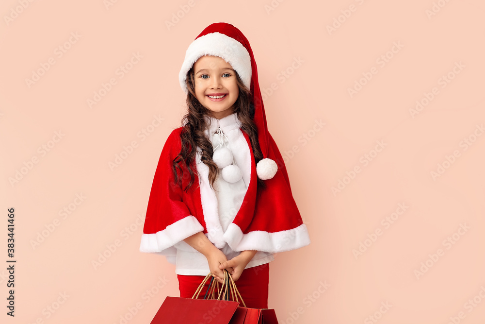 Cute little girl in Santa costume and with shopping bags on color background