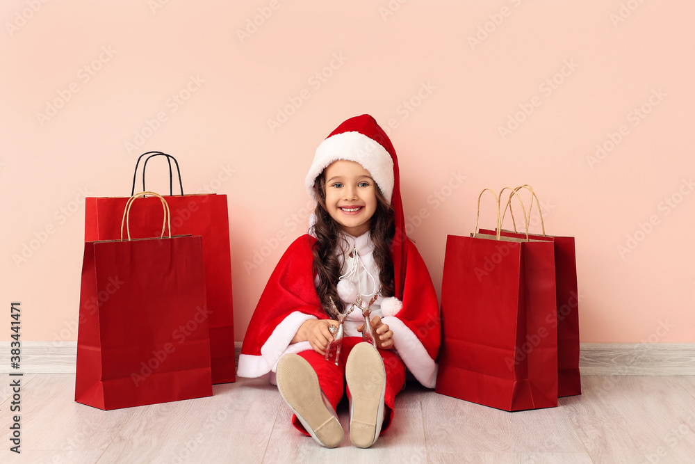 Cute little girl in Santa costume and with shopping bags near color wall