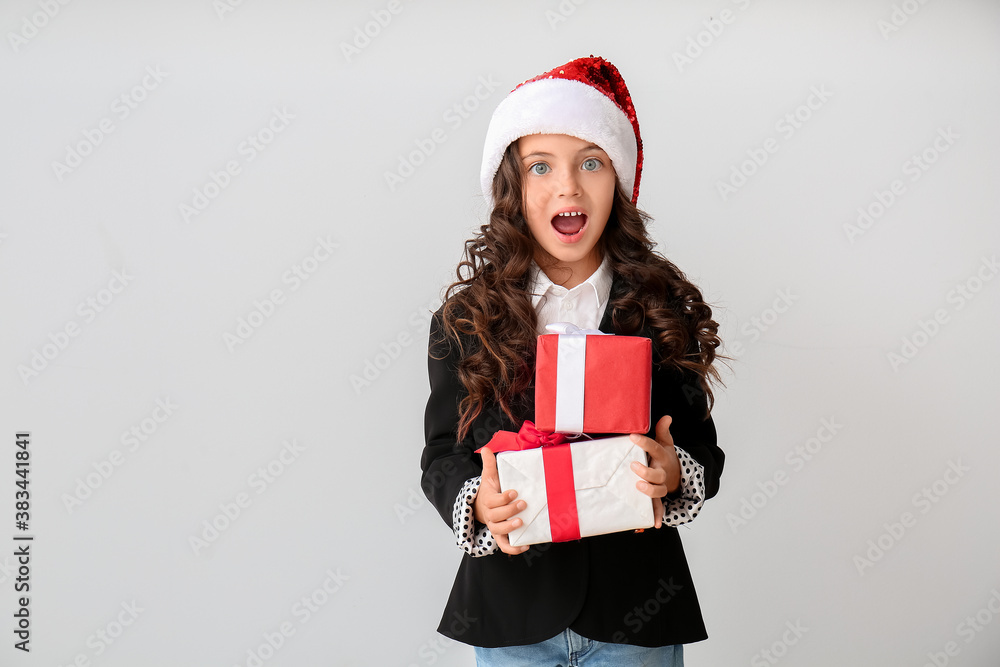 Surprised little girl in Santa hat and with gift boxes on light background