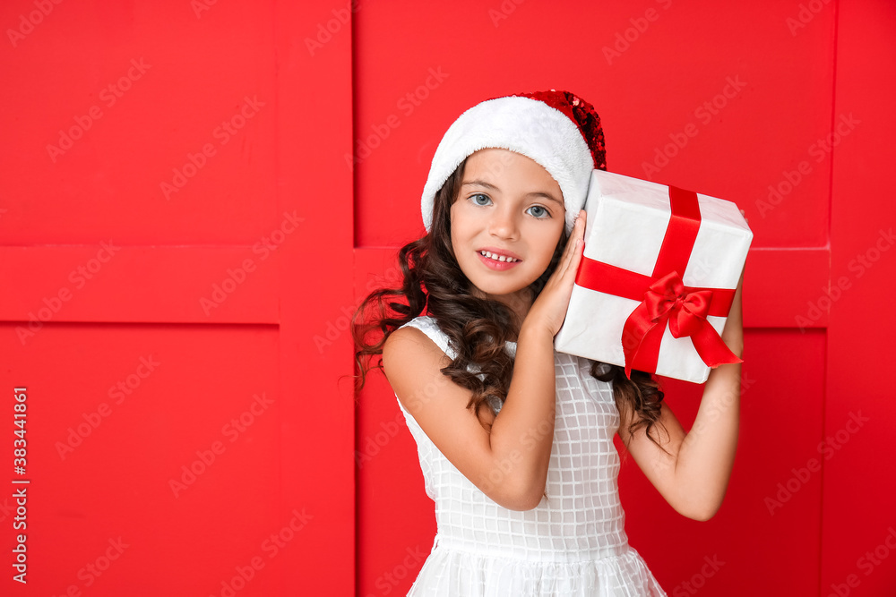 Cute little girl in Santa hat and with gift on color background