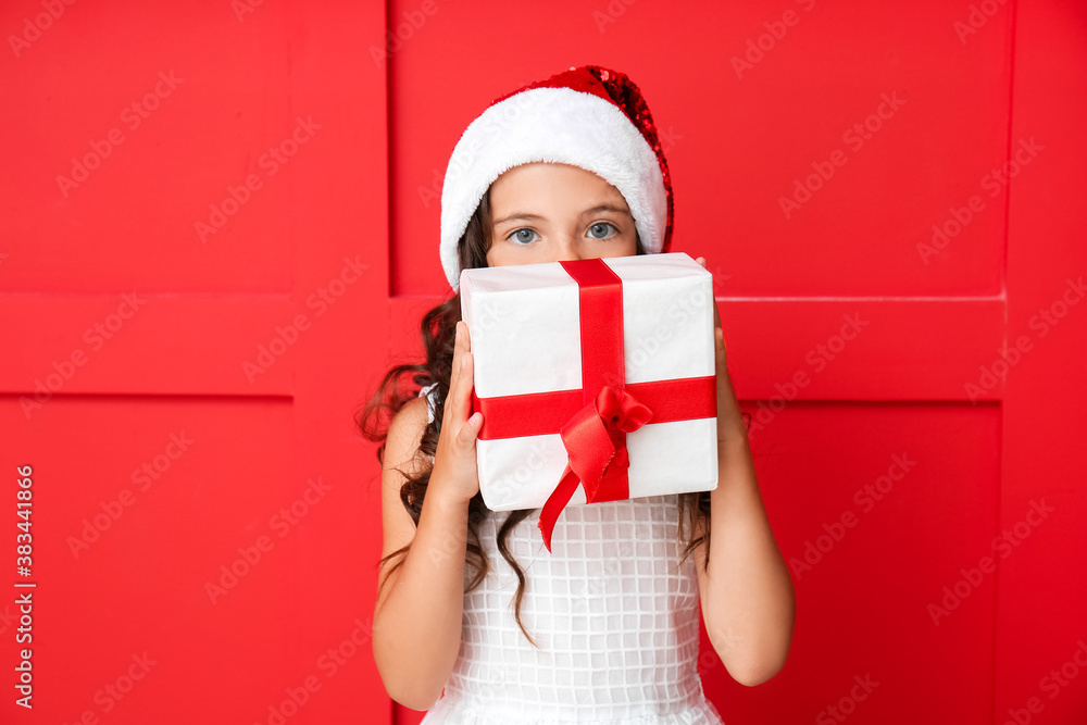 Cute little girl in Santa hat and with gift on color background