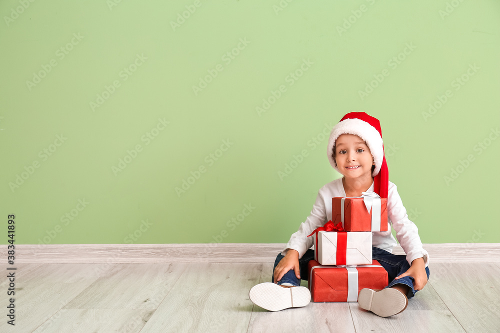 Cute little boy in Santa hat and with gift boxes near color wall