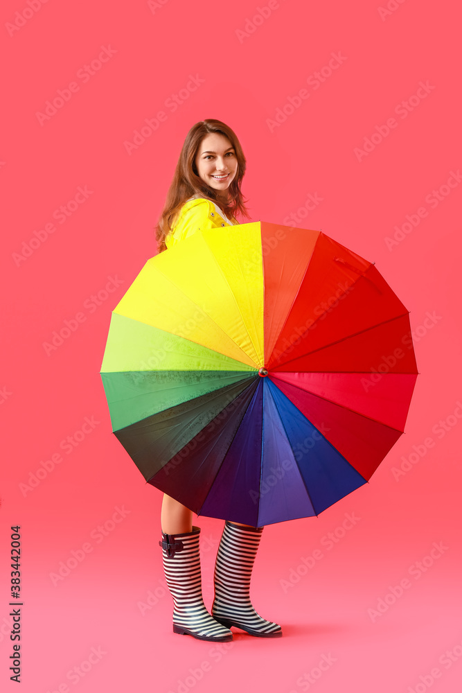 Beautiful young woman in raincoat and with umbrella on color background