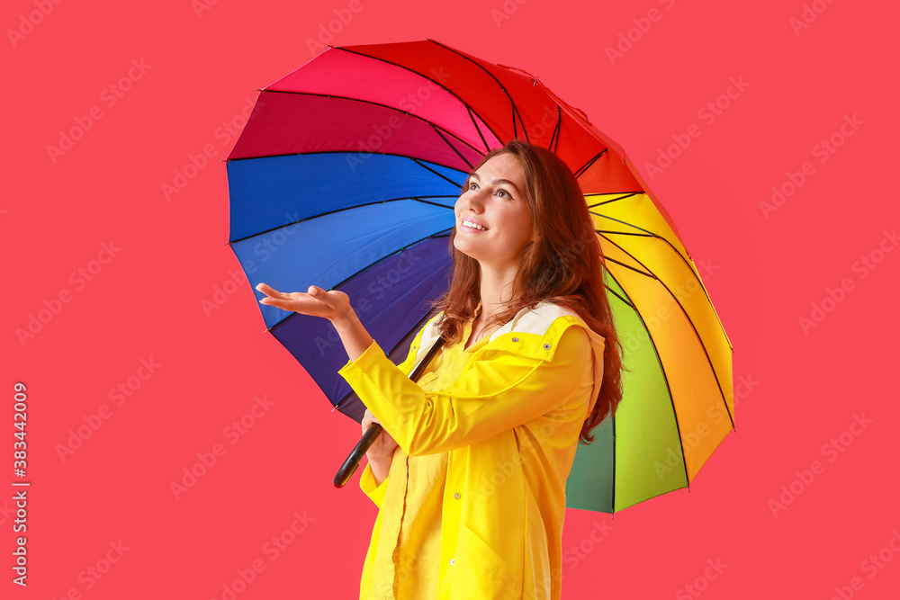 Beautiful young woman in raincoat and with umbrella on color background