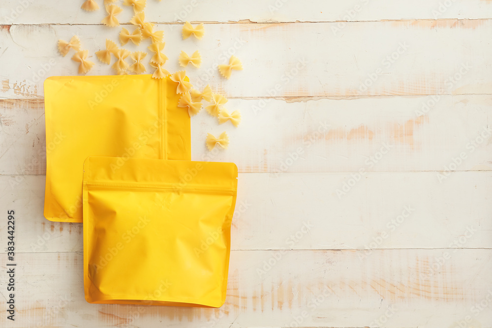 Bags with pasta on white wooden background