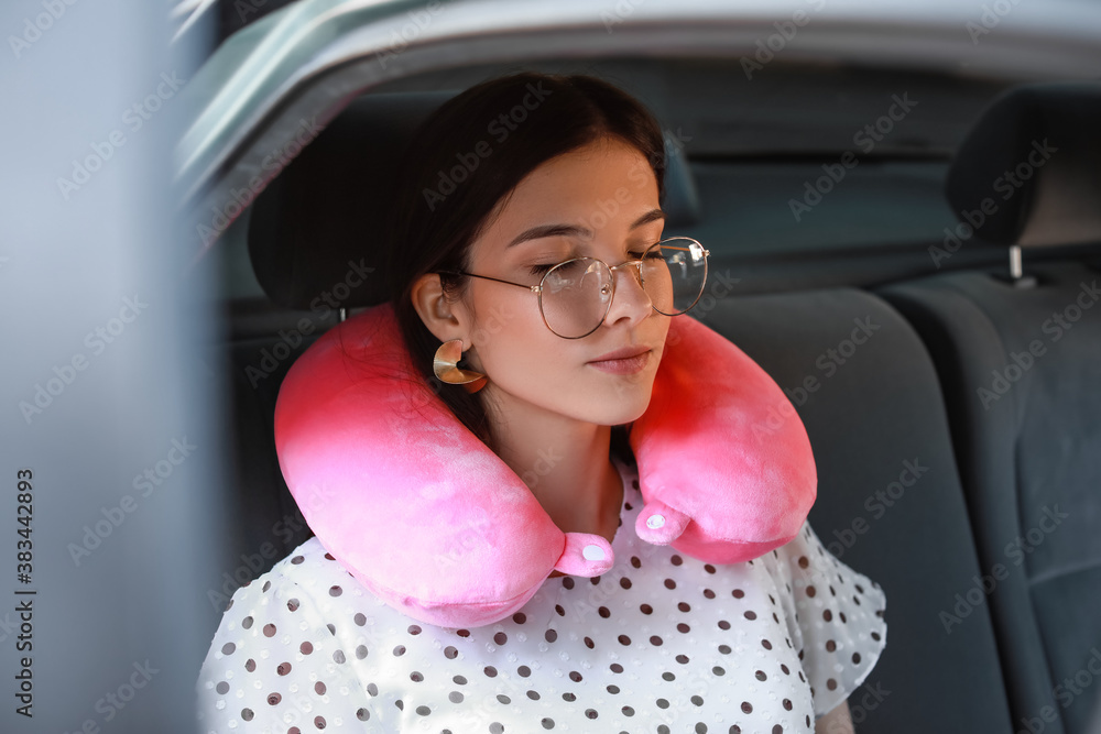 Beautiful young woman with travel pillow sitting in car