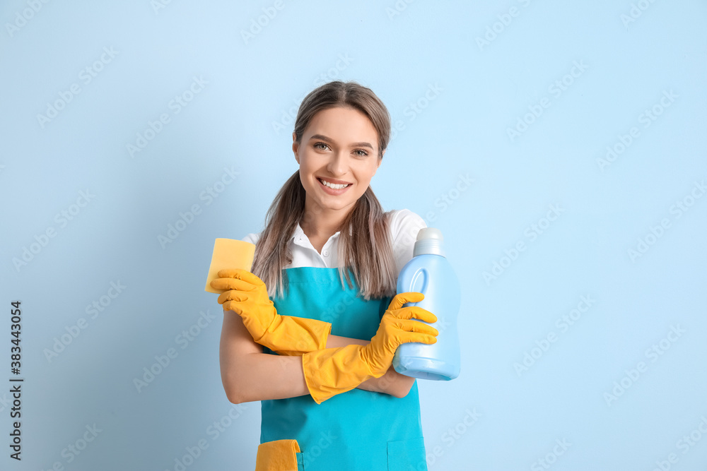 Young woman with cleaning supplies on color background