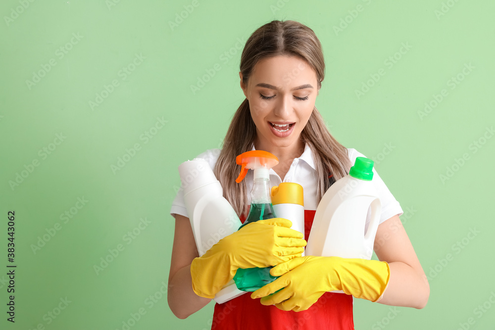 Young woman with cleaning supplies on color background