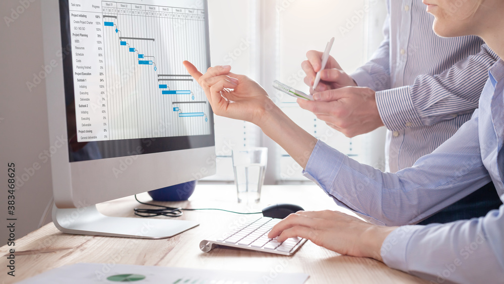 Project management team updating planning schedule with Gantt chart on computer at the office to com