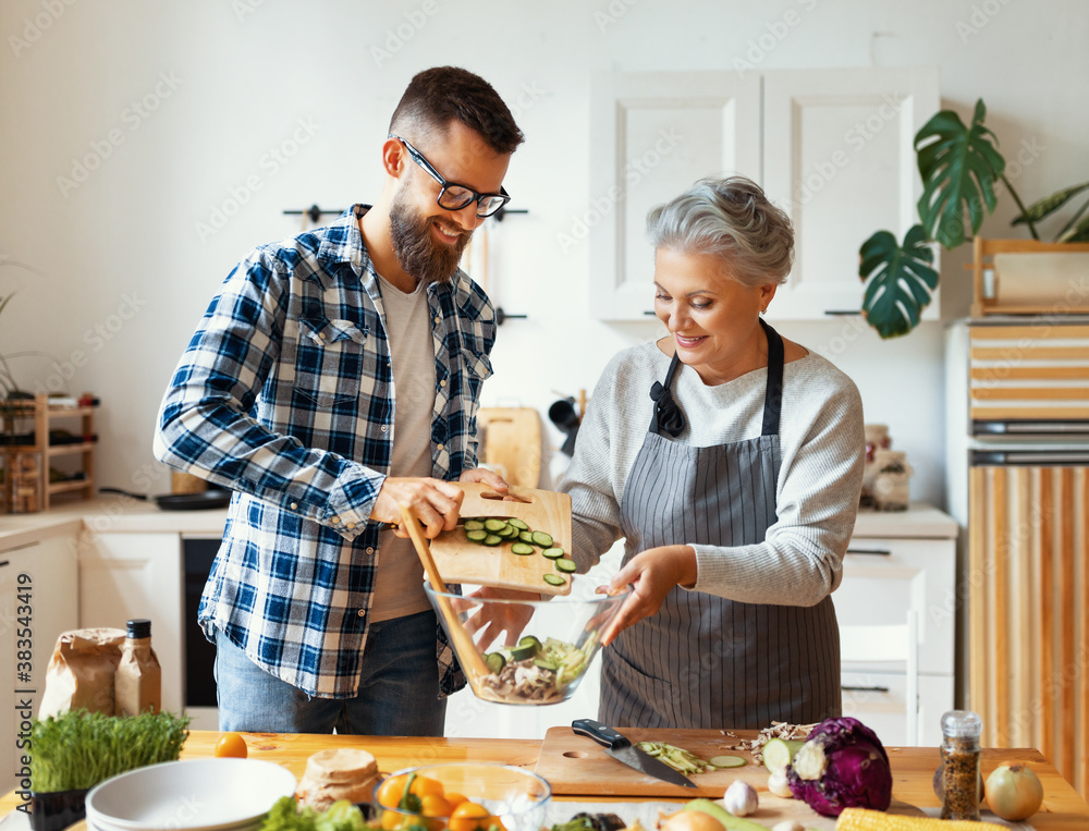 Happy mature woman with adult son cooking together at home.