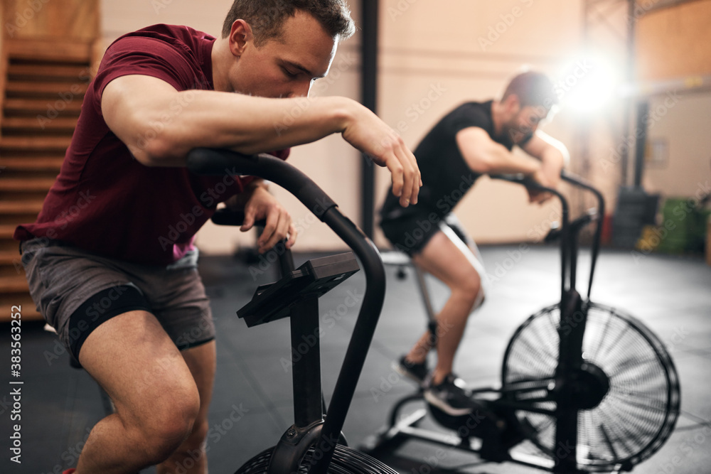 Two fit young men exhausted from a stationary bike workout