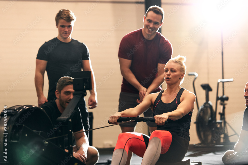 Young woman surrounded by friends while using a rowing machine