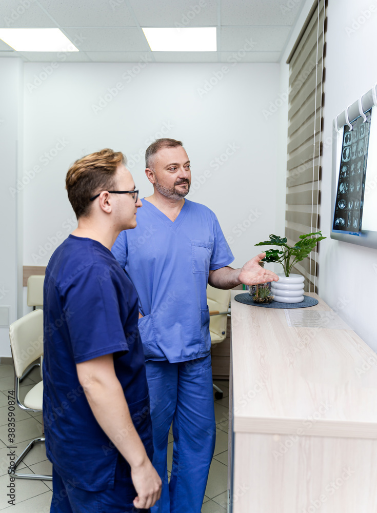 Doctors are examining x-ray of a patient. Male radiologists standing near enlighted board. Medical o