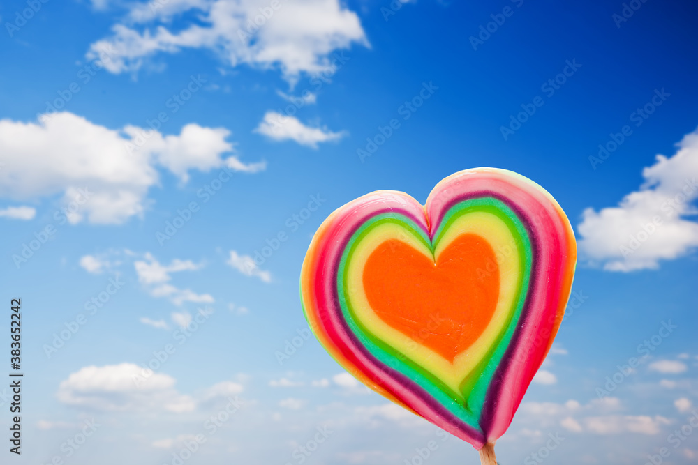 Colorful heart shaped lollipop on sky background