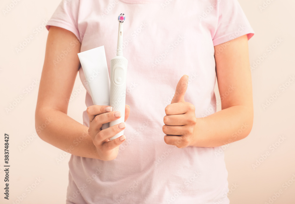 Woman with tooth brush and paste showing thumb-up on light background