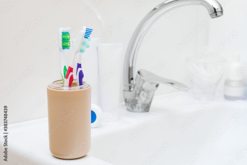 Cup with tooth brushes on sink in bathroom