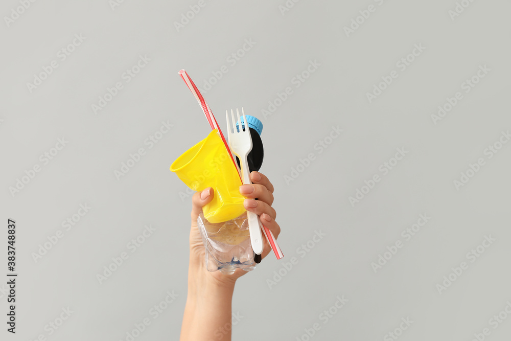 Female hand with plastic garbage on grey background. Ecology concept