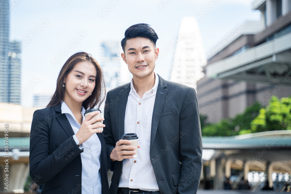 Asian young businessman and woman holding a cup of coffee in the city.