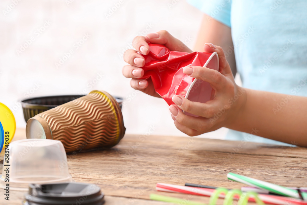 Woman crumpling plastic cup at table. Ecology concept