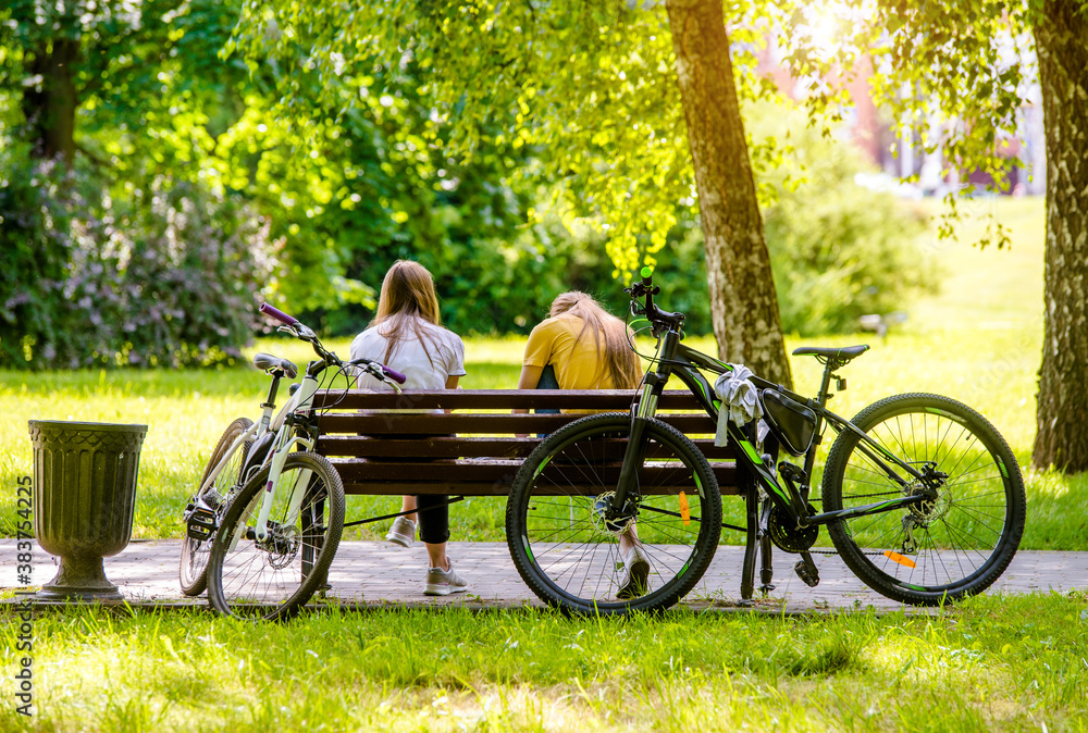 Two bicyclists rest on a Park bench
