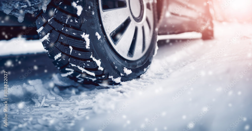 Closeup of the car tire on winter road covered with snow in snowfall in sunny day