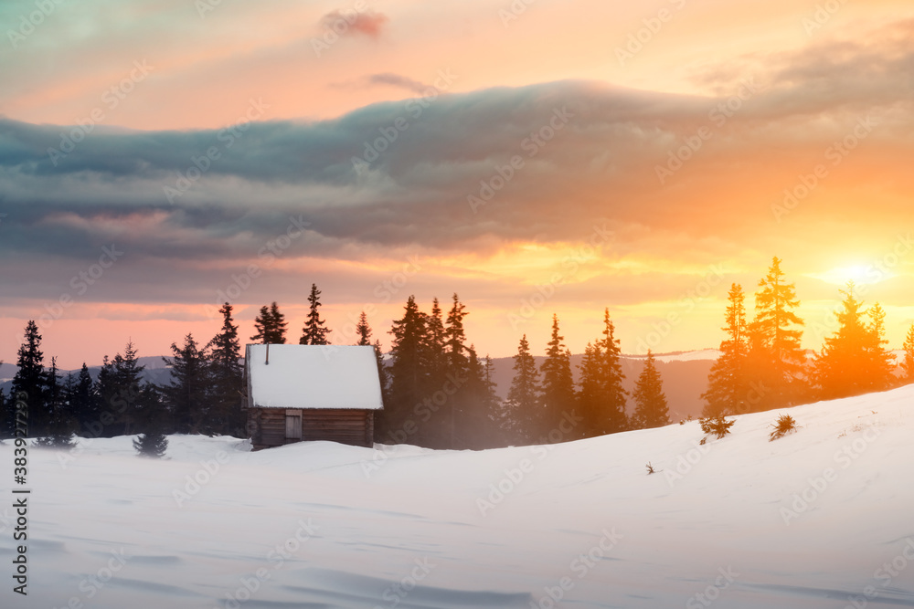 Fantastic winter landscape with wooden house in snowy mountains. Hight mountain peaks in foggy sunse