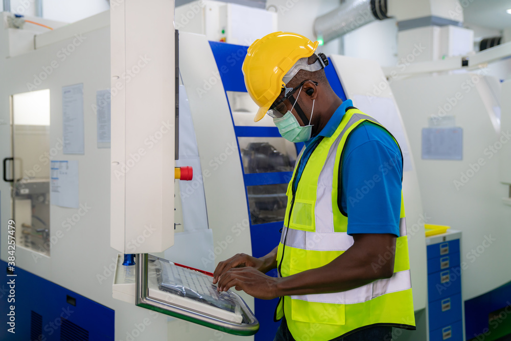 Mechanical technician with mask operative entering data in cnc milling cutting machine at factory at