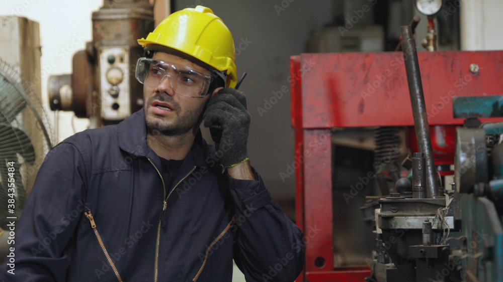 Factory worker talking on portable radio while inspecting machinery parts . Industrial and engineeri