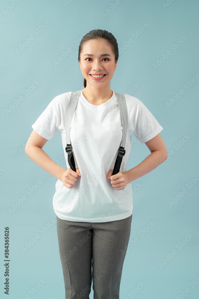 Portrait of energetic teenager girl isolated on blue background pulling forward straps of gray hipst