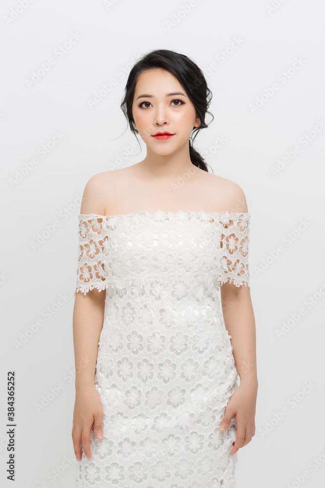 Beautiful young Asian woman with evening make-up wearing a white skinny dress over white background.