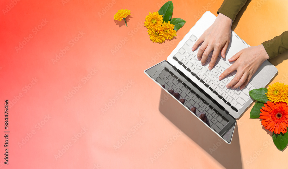 Person using a laptop computer with autumn flowers - overhead view